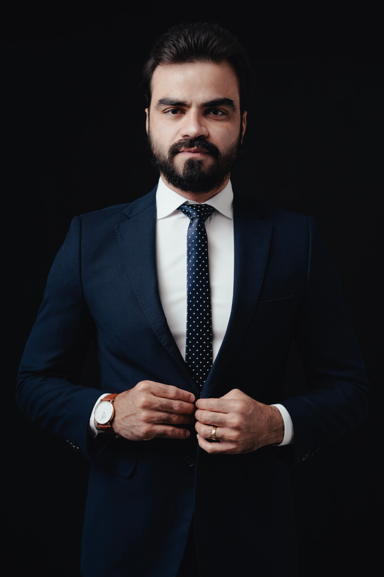 Retrato editorial de homem de terno azul-marinho, camisa branca e gravata com estampa de bolinhas, fundo preto, fotografado por Lucian Rabello