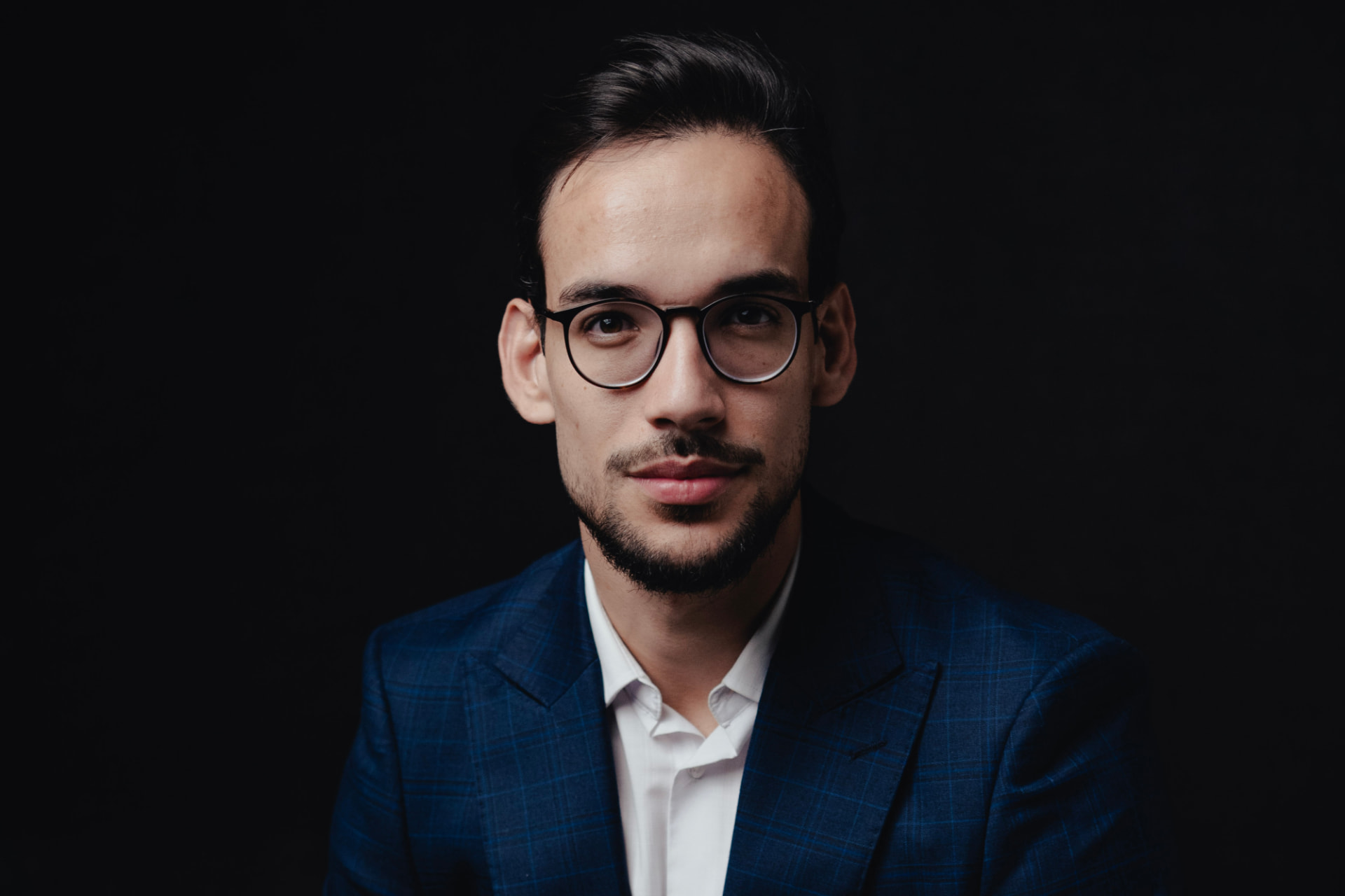 Retrato editorial de Lucian Rabello de terno azul xadrez, fundo preto