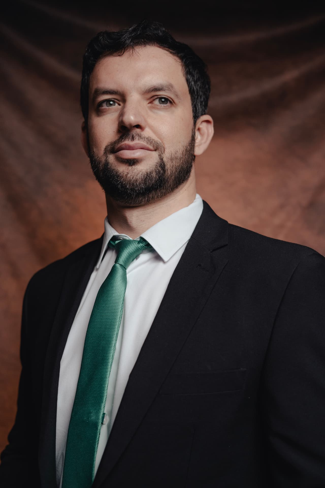 Retrato editorial de homem de terno escuro, camisa branca e gravata verde, fundo marrom texturizado, fotografado por Lucian Rabello